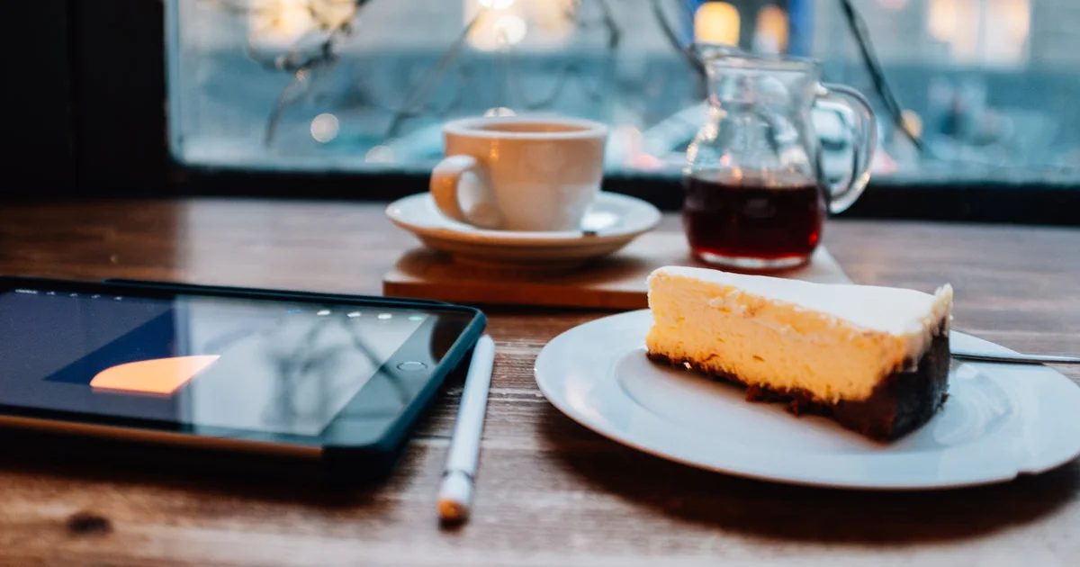 Tablet, café y una porción de torta sobre la mesa de una cafetería